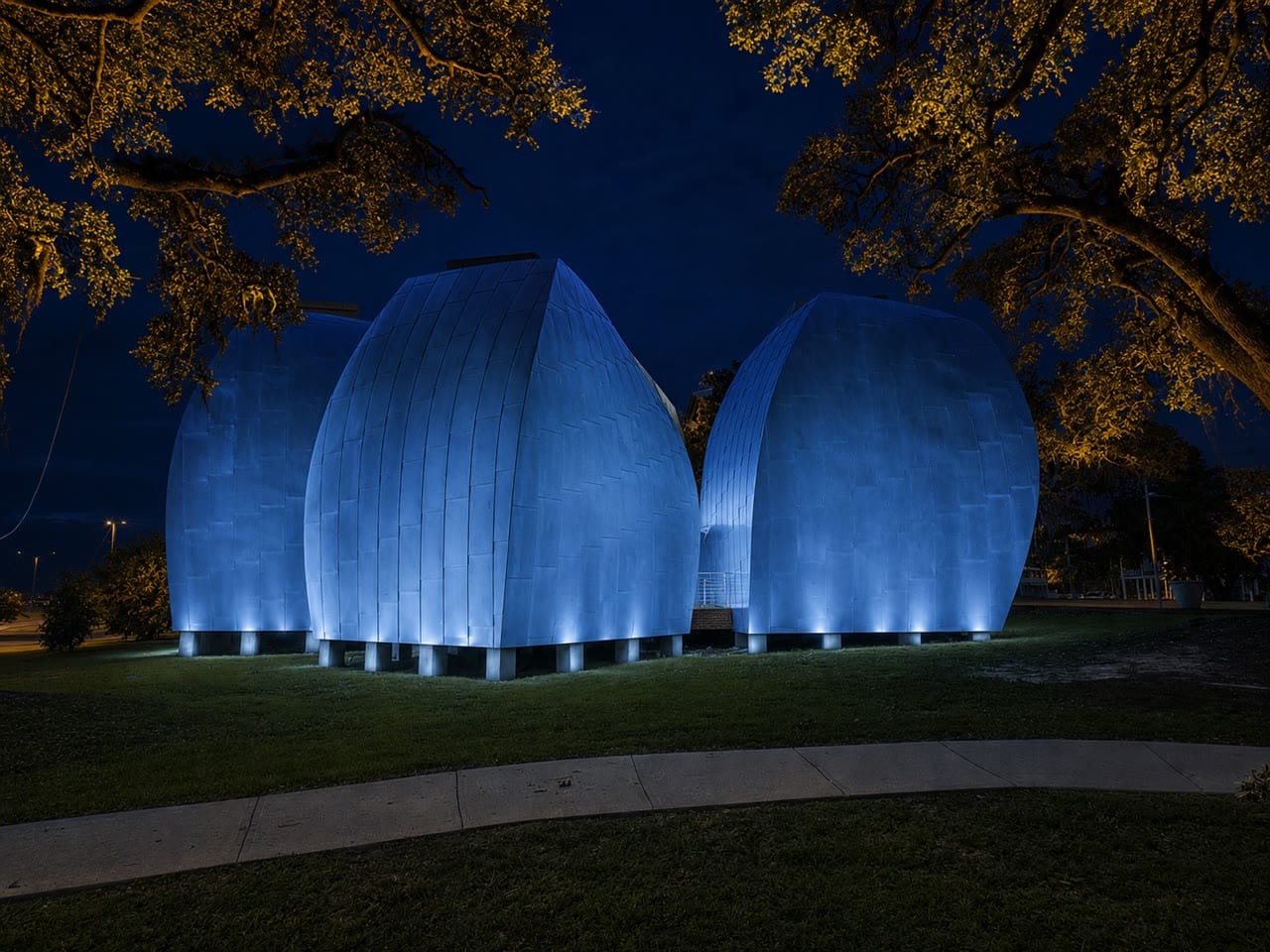 George Ohr Museum pods in steel blue uplighting beneath the oak canopy
